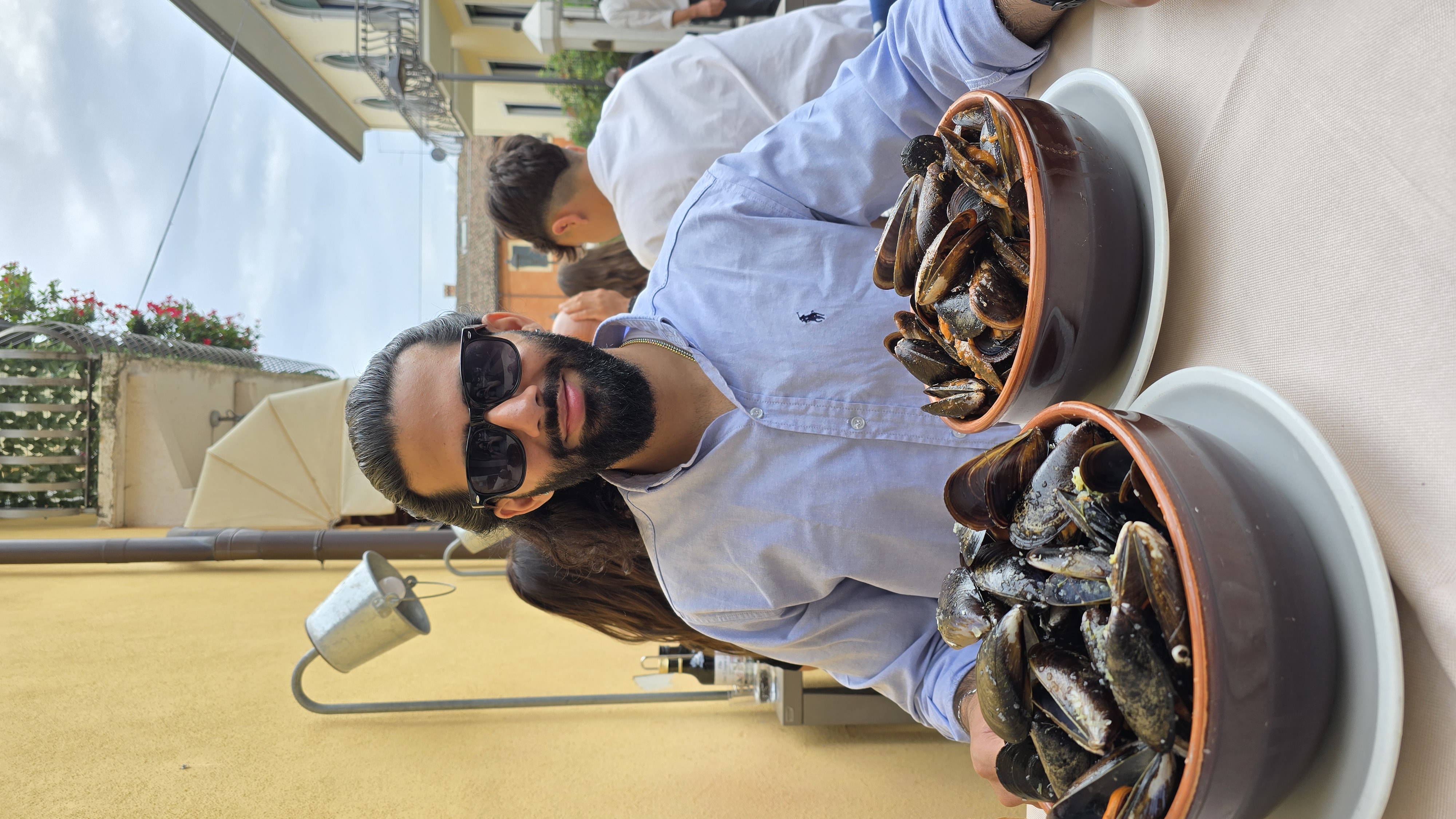 Rizwan Mahmood in Italy, holding two bowls of fresh mussels on a rooftop terrace